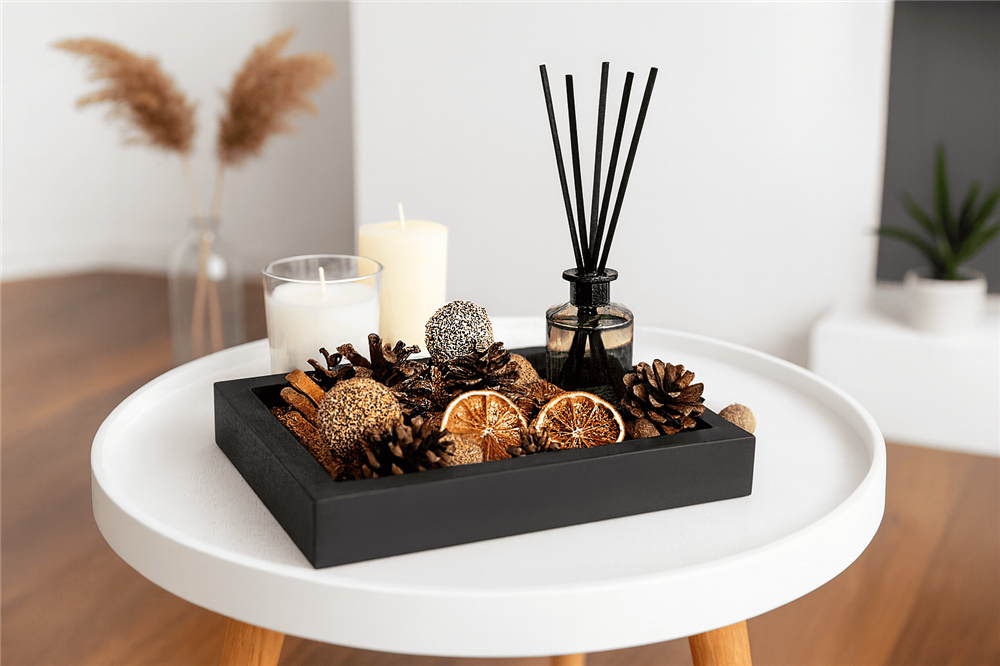 Reed diffuser placed in a decorative tray with dried citrus slices, pinecones, and candles on a round table.